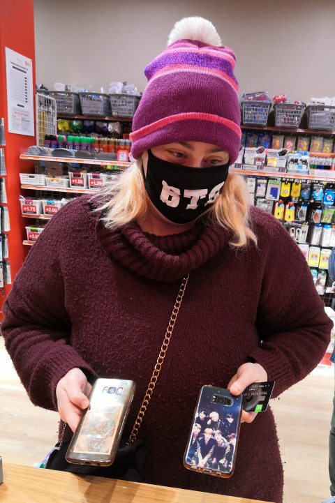 BTS 글자가 새겨진 마스크를 쓰고 휴대폰에 코팅한 BTS 사진을 보여주는 한 뉴질랜드인